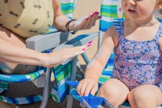 A Person Applying Sunscreen on a Young Girl's Arm